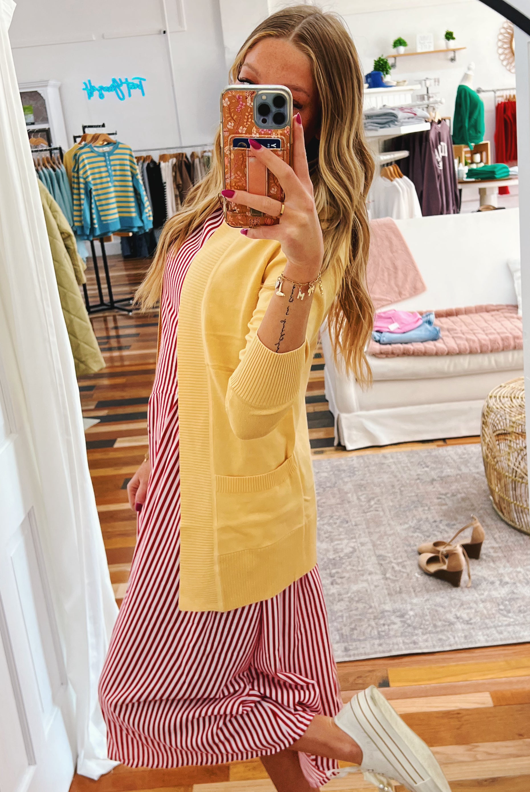 Person wearing a yellow cardigan over a pink and white striped dress in a store setting.