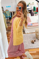 Person wearing a yellow cardigan over a pink and white striped dress in a store setting.